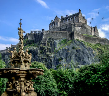 Edinburgh Castle på vulkansk klippe med smuk fontæne i Princes Street Gardens, Skotland
