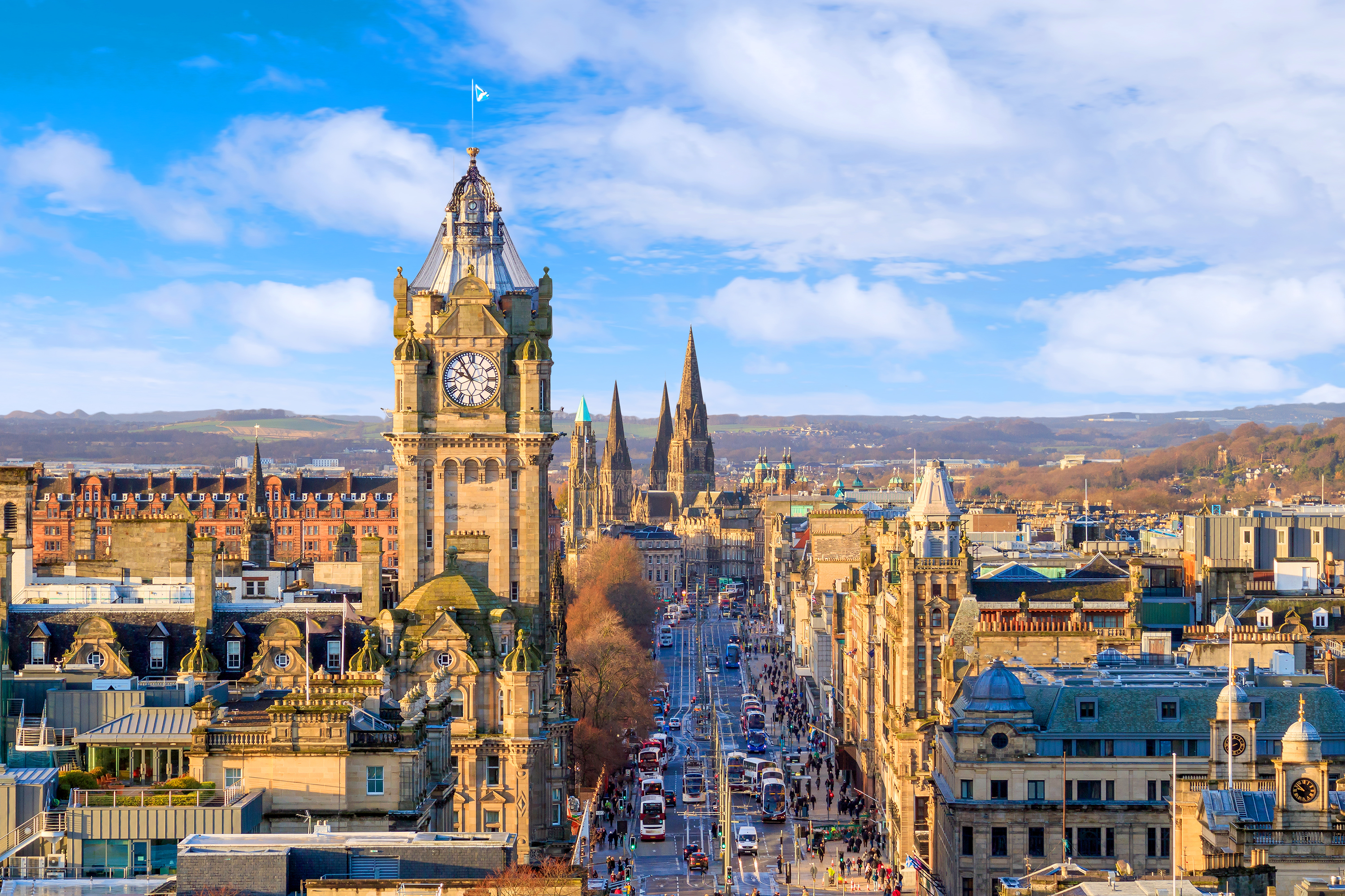 Panoramisk udsigt over Edinburghs historiske gamle bydel med karakteristiske sandstensbyggerier, klokketårn og Royal Mile under en klar blå himmel