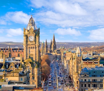 Panoramisk udsigt over Edinburghs historiske gamle bydel med karakteristiske sandstensbyggerier, klokketårn og Royal Mile under en klar blå himmel