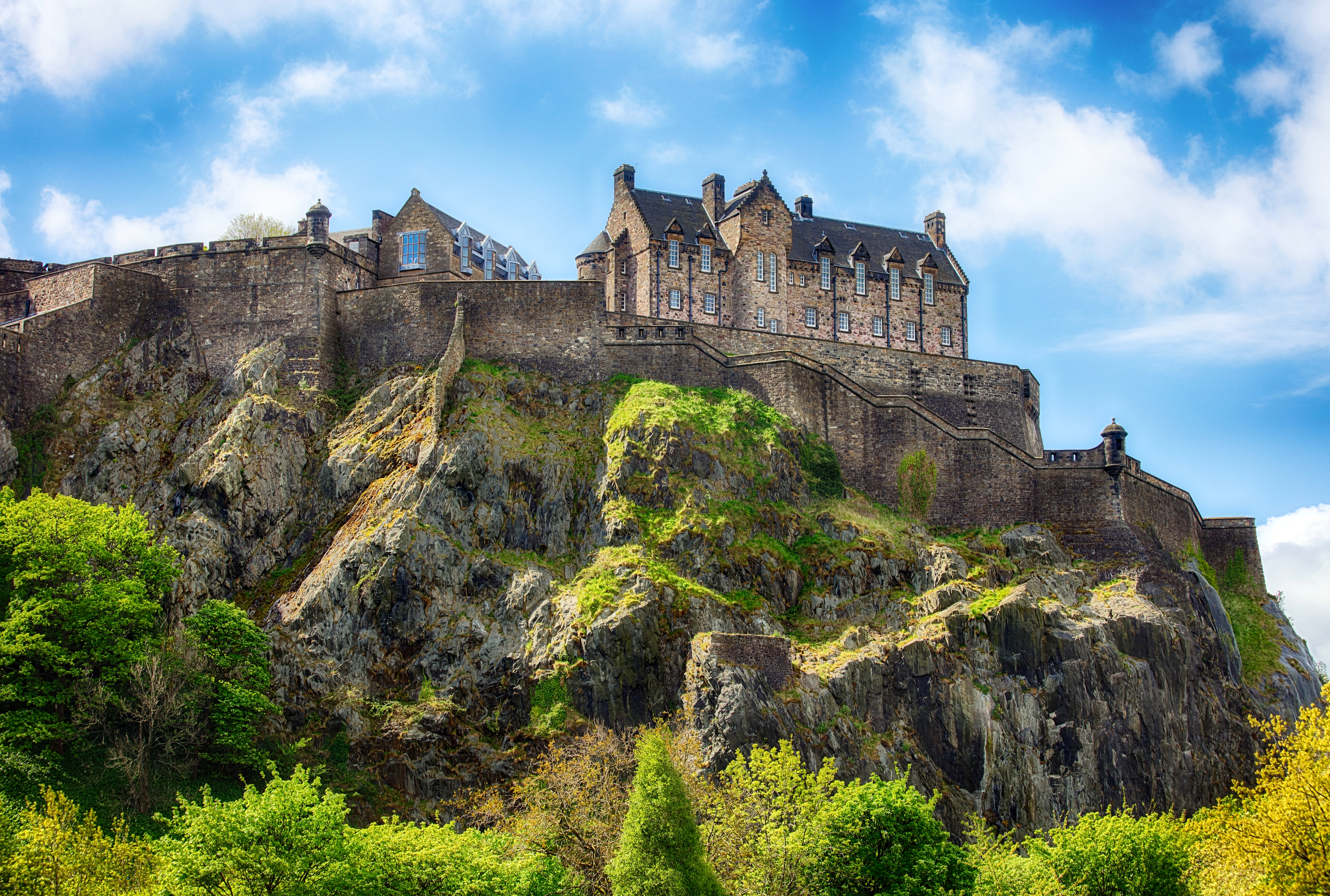 Det historiske Edinburgh Castle troner majestætisk på Castle Hill med grønne skråninger og en klar blå himmel, et ikonisk vartegn for Skotlands hovedstad