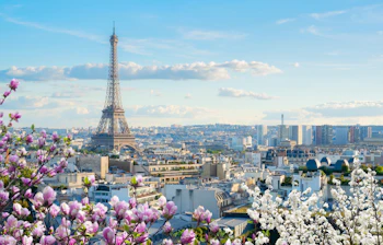 Det majestætiske Eiffeltårn der knejser over de klassiske parisiske hustage med en klar blå himmel som baggrund, symbolet på romantiske Paris