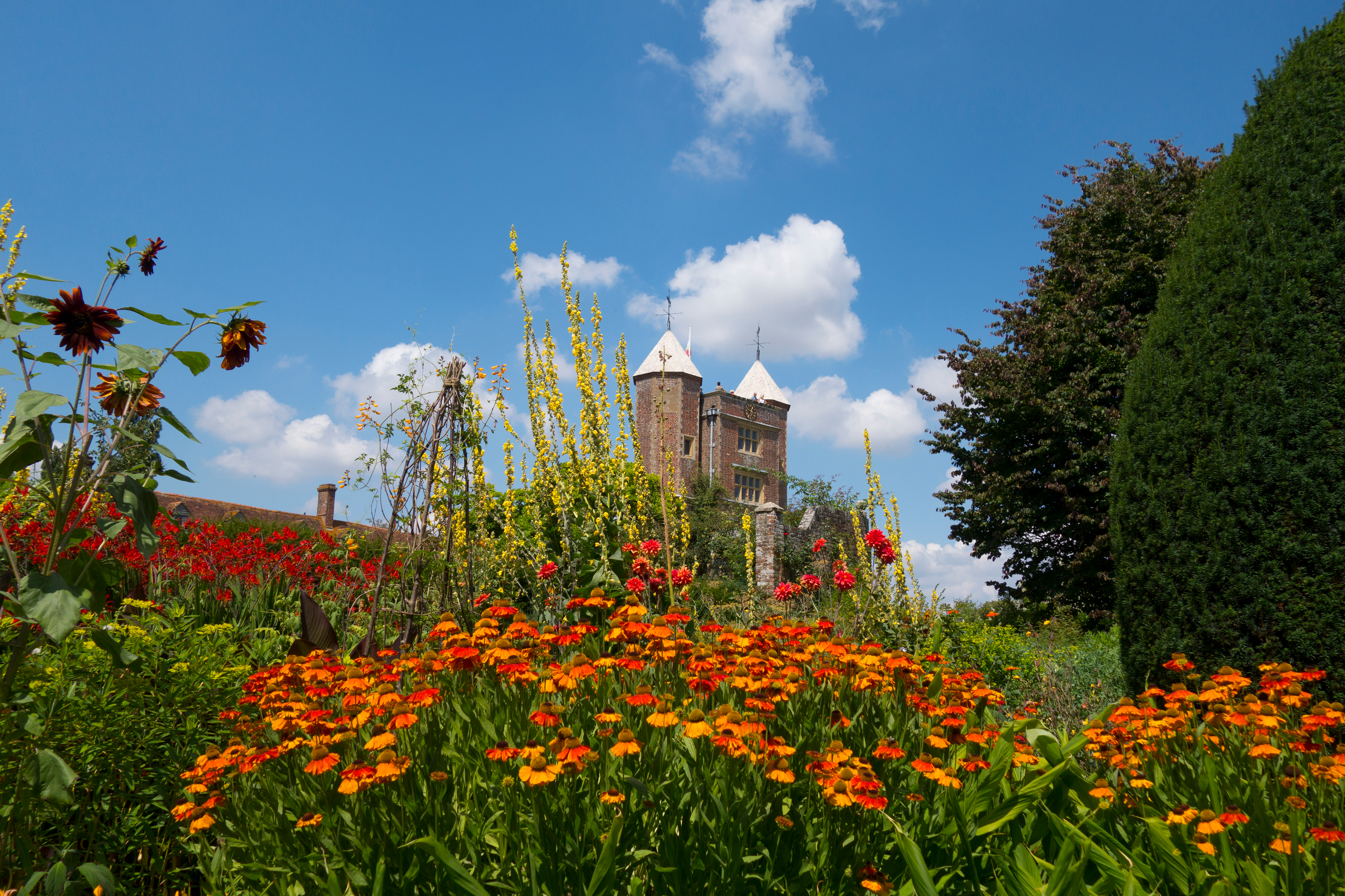Historisk borgtårn med farverig have fuld af orange og røde blomster under blå himmel