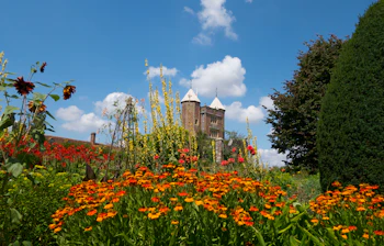 Historisk borgtårn med farverig have fuld af orange og røde blomster under blå himmel