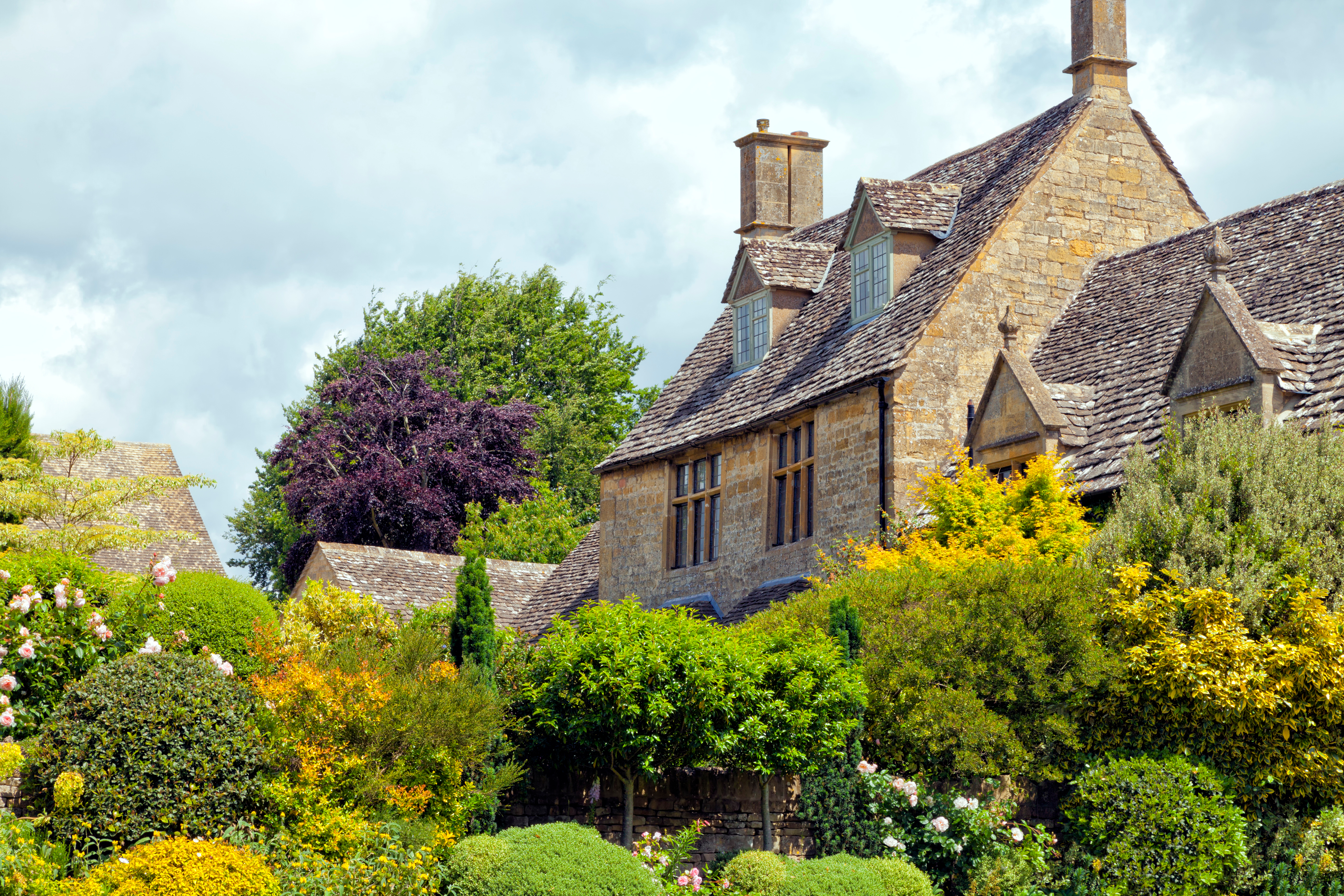 Traditionelt engelsk cottage med kalkstenmure og blomstrende have i Cotswolds