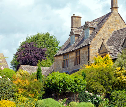 Traditionelt engelsk cottage med kalkstenmure og blomstrende have i Cotswolds