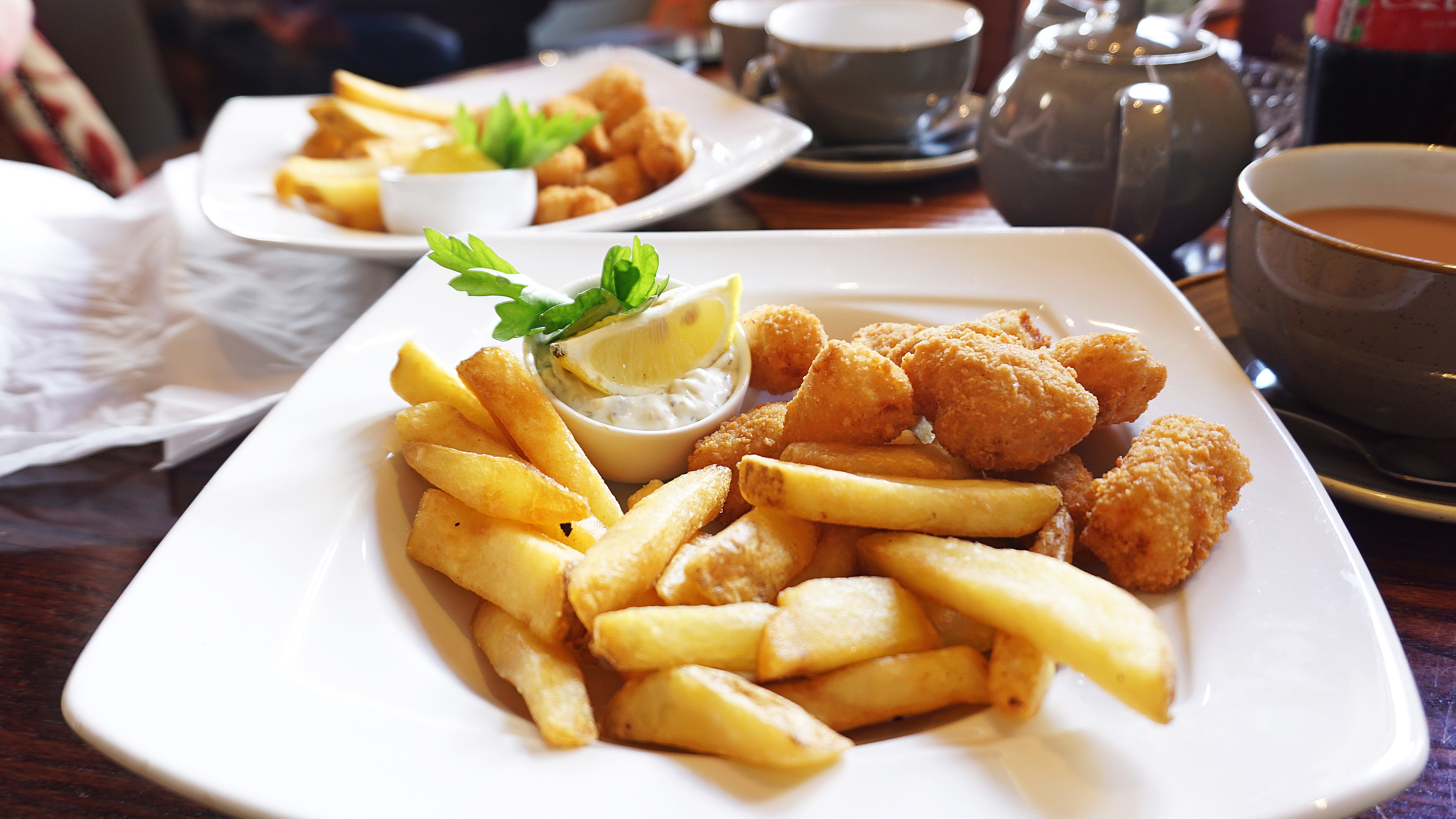 Traditionel engelsk fish and chips med scampi serveret på hvid tallerken med tartarsauce og citron