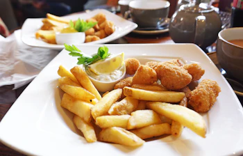 Traditionel engelsk fish and chips med scampi serveret på hvid tallerken med tartarsauce og citron