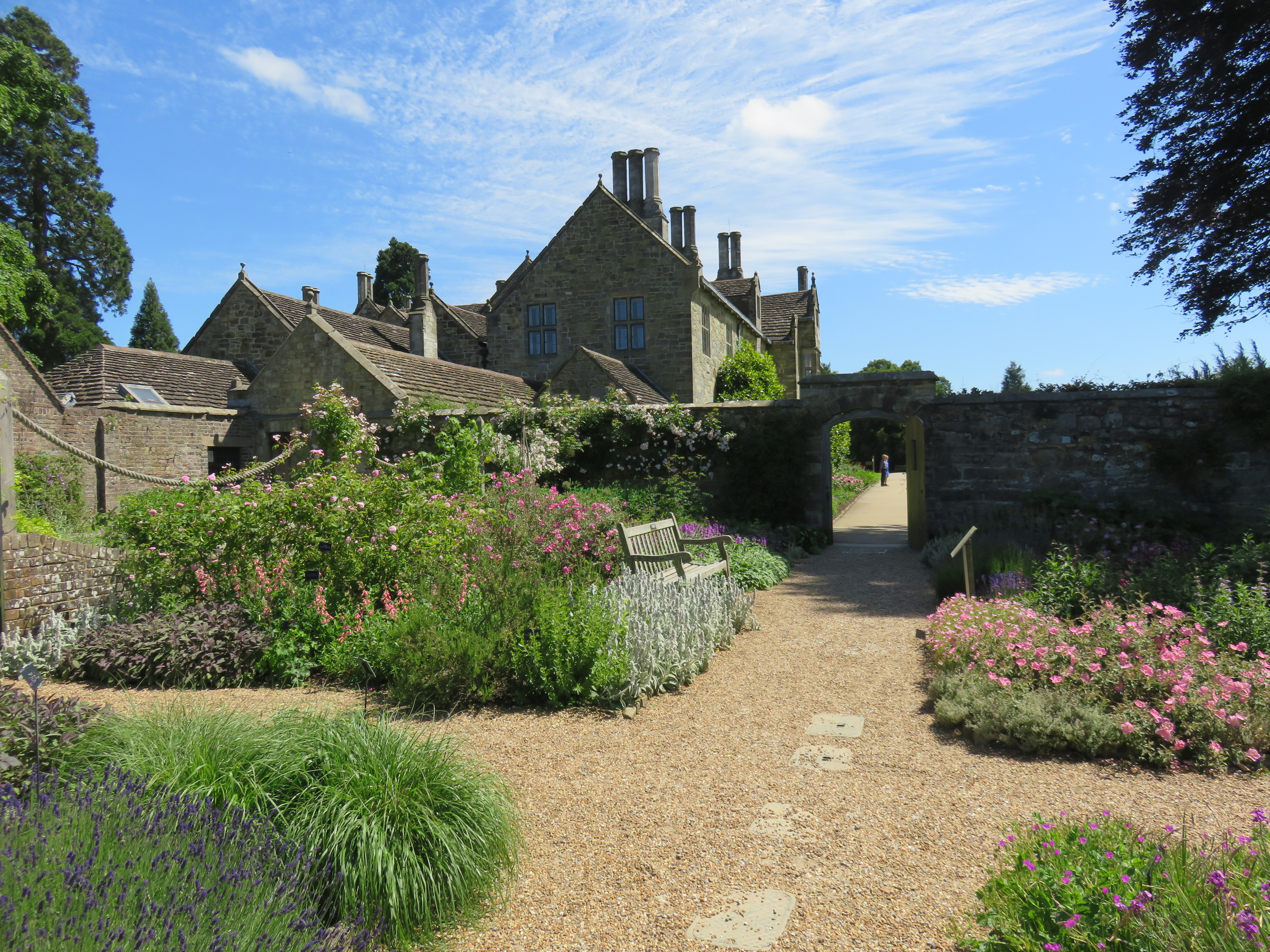 Smuk indhegnet have ved engelsk herregård i Sussex med farverige blomsterbede, grusstier og historisk stenarkitektur under en blå sommerhimmel