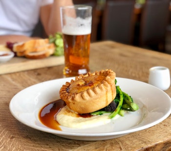 Traditionel engelsk pie and mash med sauce, grøntsager og et glas øl serveret i autentisk gastropub miljø i England