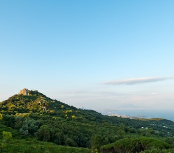 Eremo di San Nicola på toppen af Mount Epomeo på Ischia badet i gyldent aftenslys med Vesuv synlig i horisonten