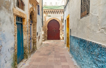 Charmerende smal gade i Essaouiras historiske Medina med traditionel marokkansk arkitektur, hvidkalkede mure, blaa detaljer og en dekorativ doer