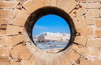 De historiske fæstningsværker i Essaouira med udsigt over de blå fiskerbåde i havnen ved Atlanterhavet i Marokko