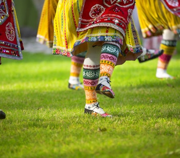Farverige estiske folkedansere i traditionelle nationaldragter med mønstrede sko under kulturfestival i Tallinn