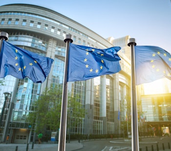 Europæiske Unions flag vajer foran EU-Parlamentets imponerende glasfacade i Bruxelles under en solrig dag