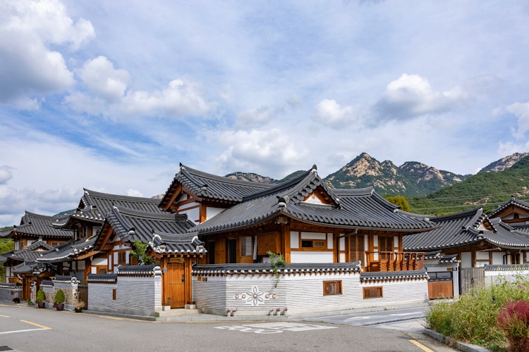 Idyllisk udsigt over Eunpyeong Hanok-landsbyen i Seoul med traditionelle koreanske huse med buede tage, stenbelagte stier og smukke bjerge i baggrunden