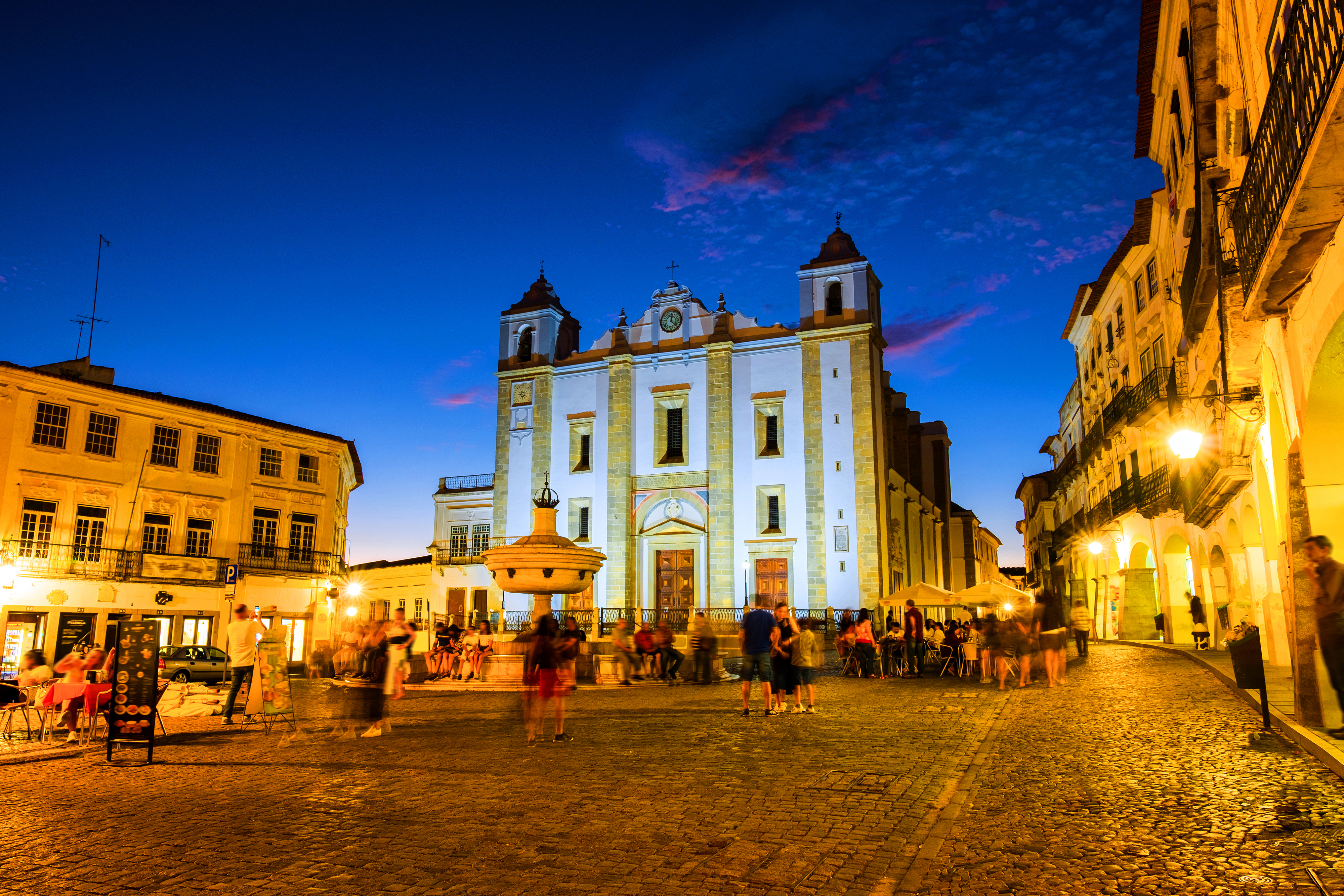 Praça do Giraldo i Évora ved solnedgang med det oplyste katolske domkirke og springvand omgivet af turister i Portugal