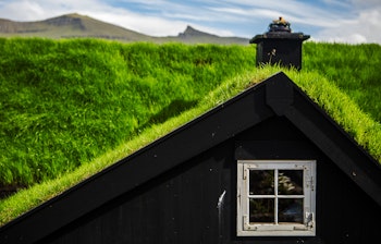 Traditionelt færøsk hus med grønt græstag og hvidt vindue i Kirkjubøur på Streymoy, Færøerne