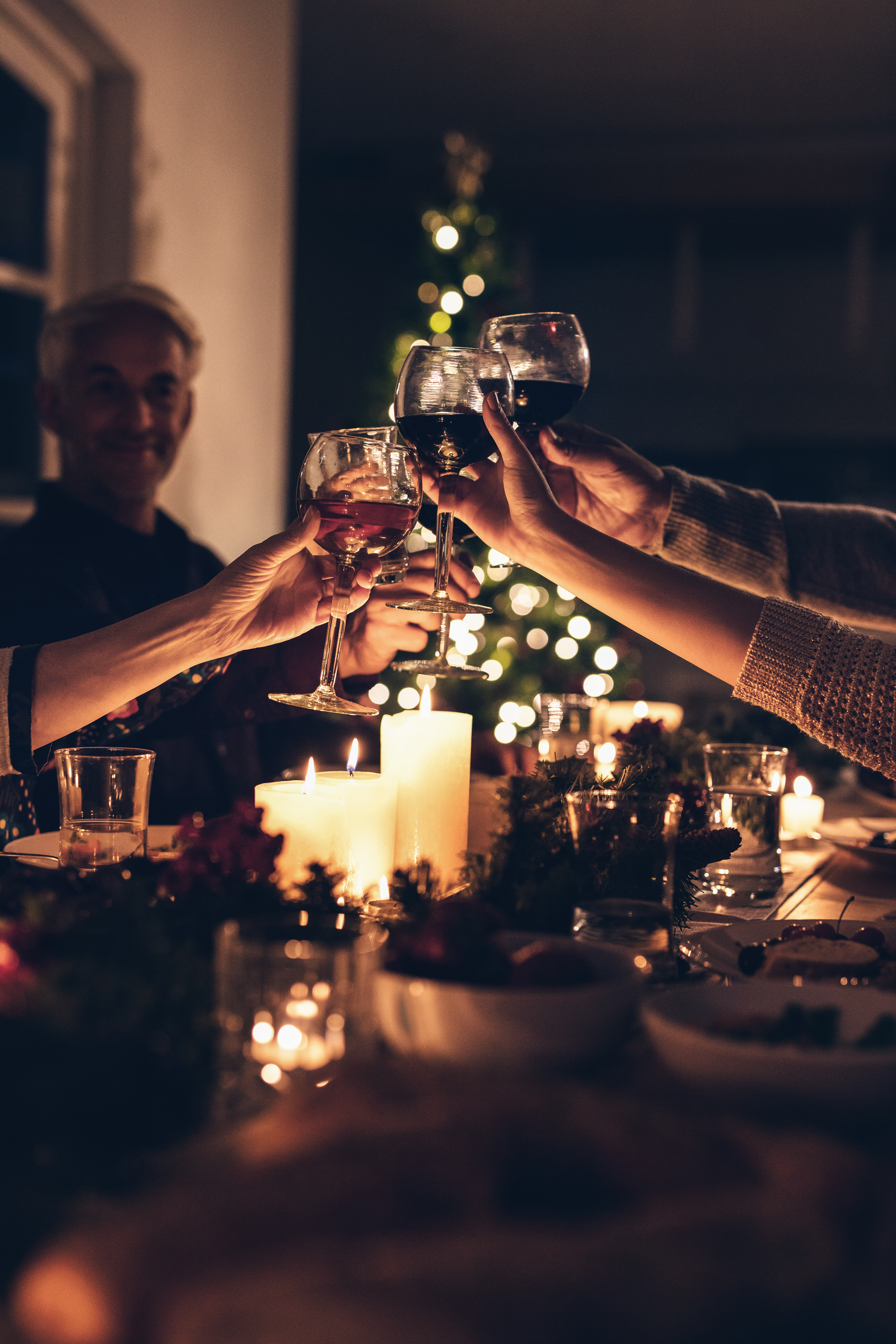 Nærbillede af familiemedlemmers hænder der skåler med vinglas ved en hyggelig julemiddag, som indfanger varmen og samhørigheden ved flergenerationers festlige sammenkomst