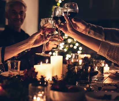 Nærbillede af familiemedlemmers hænder der skåler med vinglas ved en hyggelig julemiddag, som indfanger varmen og samhørigheden ved flergenerationers festlige sammenkomst