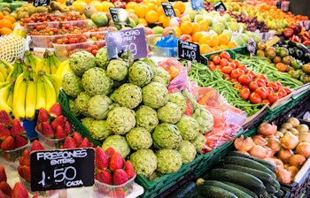 Farverig frugt- og grøntsagsbod på det berømte La Boqueria marked i Barcelona med friske jordbær, appelsiner og tomater