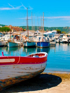 Malerisk udsigt over den farverige havn i Saint-Tropez med traditionelle fiskerbåde og sejlbåde fortøjet ved solnedgang på den franske riviera