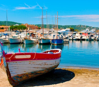 Malerisk udsigt over den farverige havn i Saint-Tropez med traditionelle fiskerbåde og sejlbåde fortøjet ved solnedgang på den franske riviera