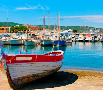 Malerisk udsigt over den farverige havn i Saint-Tropez med traditionelle fiskerbåde og sejlbåde fortøjet ved solnedgang på den franske riviera