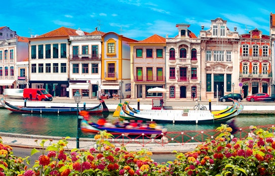 Traditionelle farverige både på kanalen i Aveiro, Portugal, med charmerende bygninger under blå himmel på en solrig sommerdag