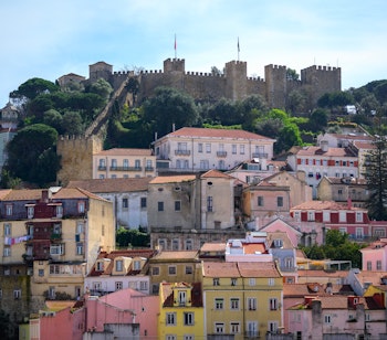 Malerisk udsigt over farverige bygningsfacader i Lissabon med det historiske Castelo de São Jorge tronende på bakken i baggrunden