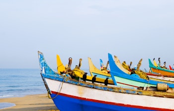 Farverige traditionelle fiskerbåde på stranden i Kovalam, Kerala, Indien med azurblåt hav og klar himmel i baggrunden