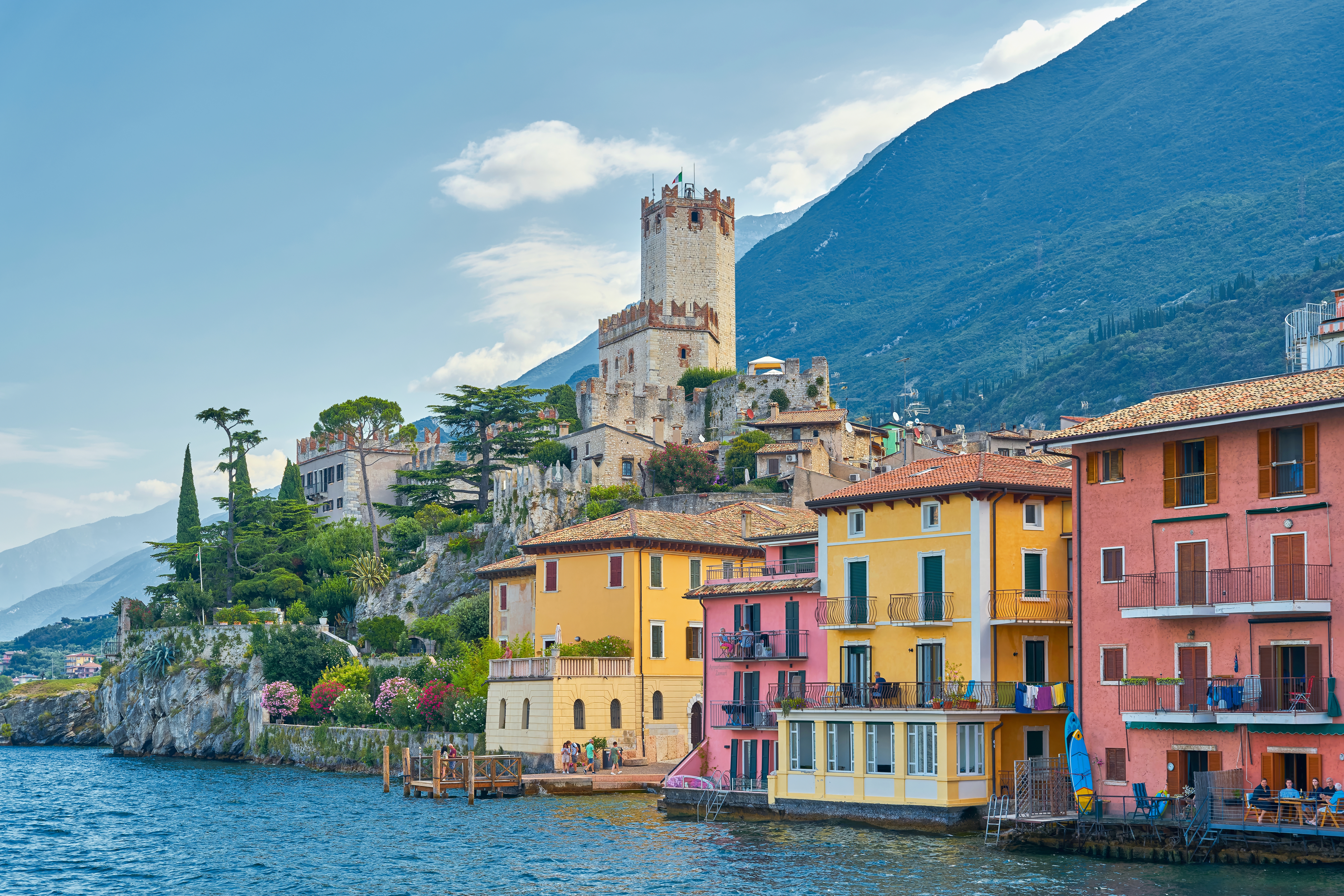 Farverige huse ved Lago di Garda med historisk tårn og bjerglandskab i Italien