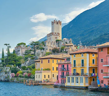 Farverige huse ved Lago di Garda med historisk tårn og bjerglandskab i Italien