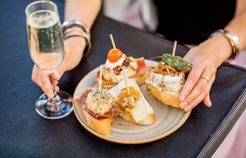 Farverige spanske pinchos og tapas serveret udendørs med et glas hvidvin - traditionel middelhavsgastronomioplevelse fra Spanien