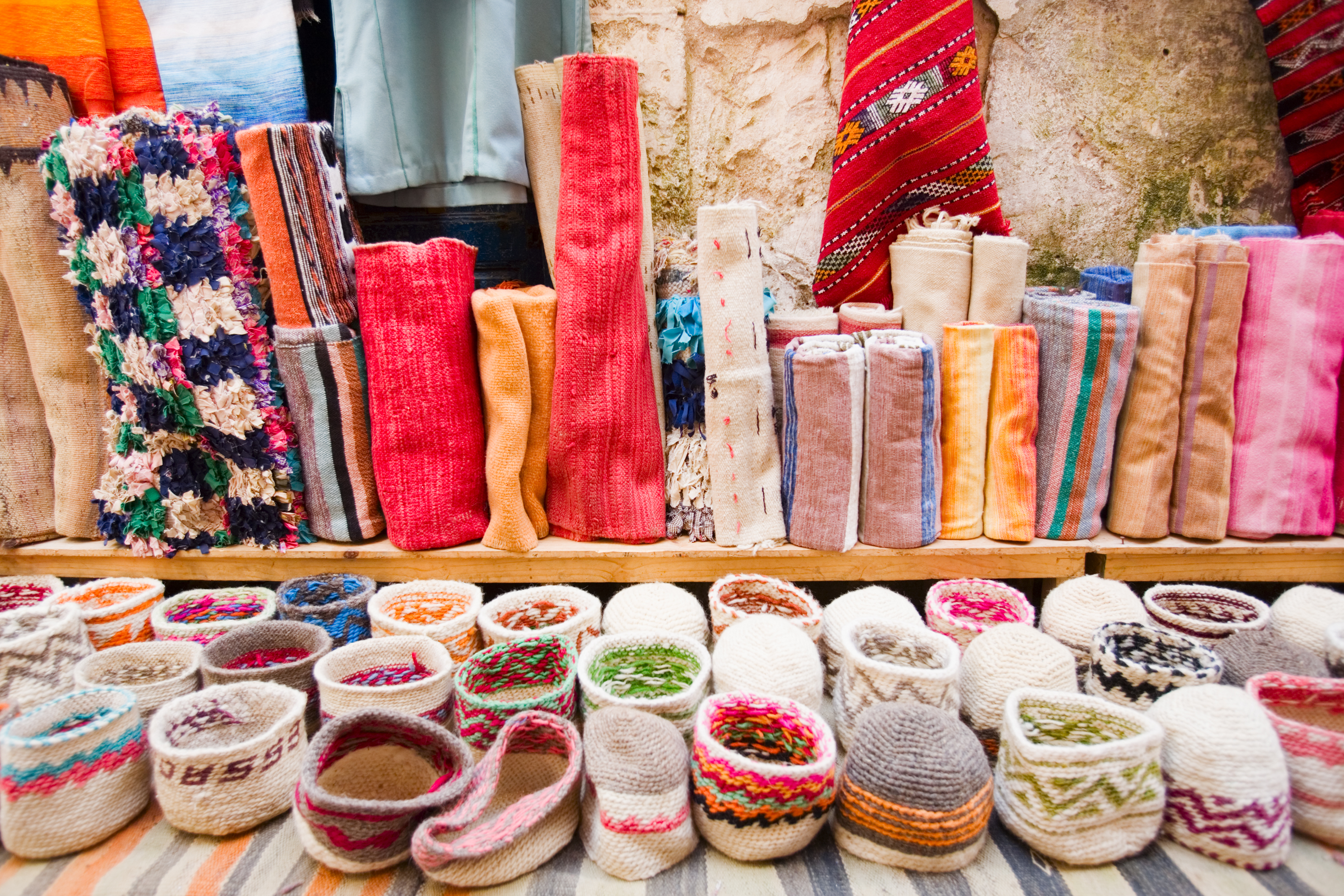 Farverige traditionelle tekstiler og håndværk på et marked i Essaouira, Marokko, med flotte tæpper og kurve