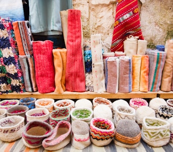 Farverige traditionelle tekstiler og håndværk på et marked i Essaouira, Marokko, med flotte tæpper og kurve