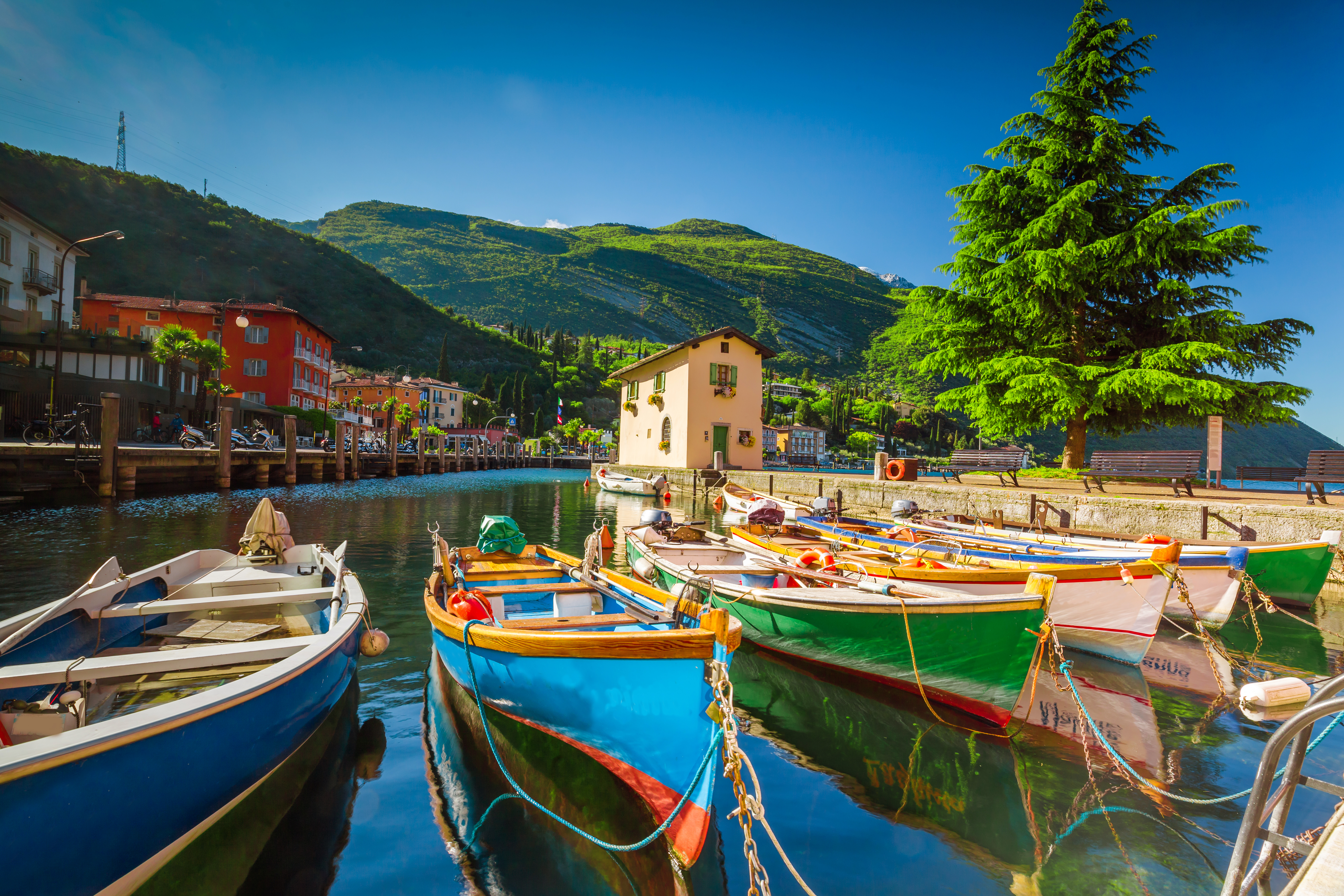 Farverige træbåde i havnen ved Torbole by ved Gardasøen med italienske bygninger og grønne bjerge i baggrunden