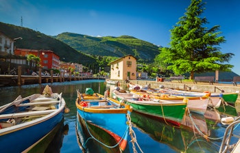 Farverige træbåde i havnen ved Torbole by ved Gardasøen med italienske bygninger og grønne bjerge i baggrunden