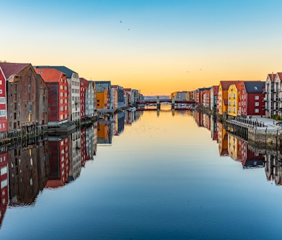 Farverige træhuse langs Nidelva-floden i Trondheims historiske Brygge-kvarter ved solnedgang med perfekte refleksioner i vandet