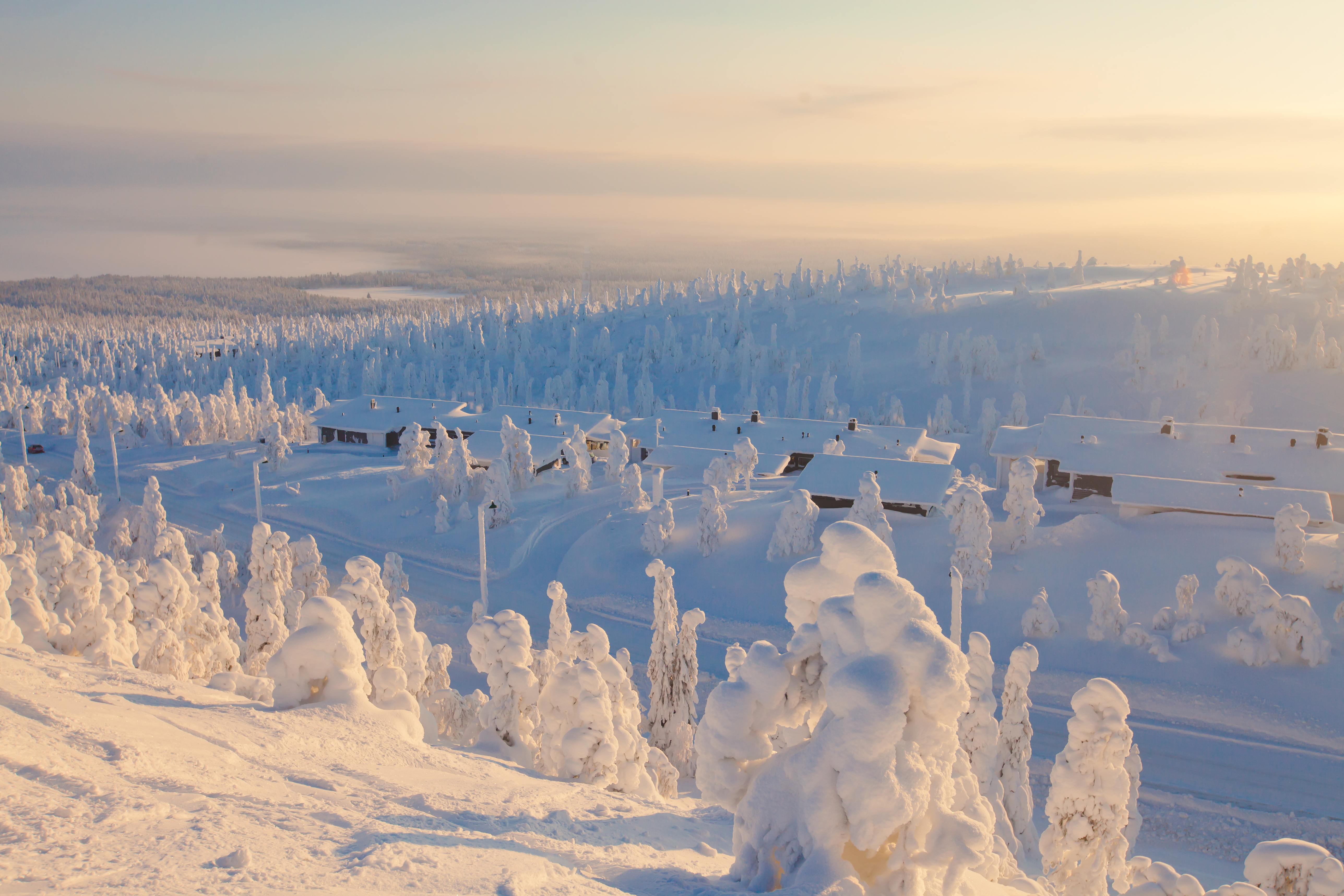 Snedækket skiresort i finsk Lapland med rimfrost på træer og vinterhytter under gyldent sollys