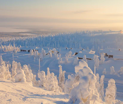 Snedækket skiresort i finsk Lapland med rimfrost på træer og vinterhytter under gyldent sollys