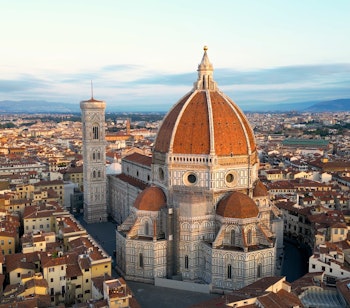 Betagende luftfoto af Firenzes domkirke (Duomo di Firenze) med dens ikoniske terrakotta-kuppel, badet i gyldent solnedgangslys over den historiske bymidte i Toscana, Italien