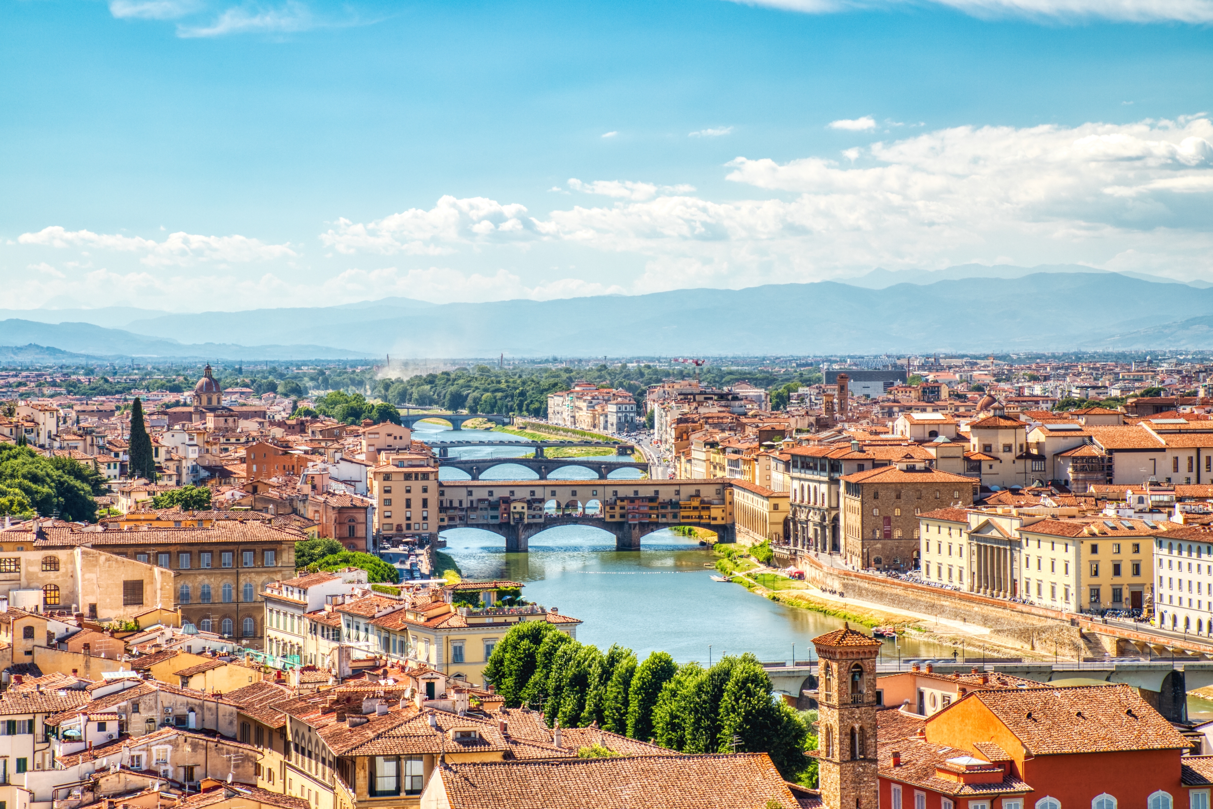 Betagende luftudsigt over den historiske Ponte Vecchio bro i Firenze med Arno-floden og byens charmerende røde tage under den toscanske sol