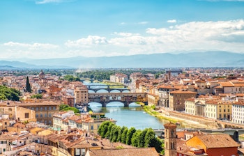 Betagende luftudsigt over den historiske Ponte Vecchio bro i Firenze med Arno-floden og byens charmerende røde tage under den toscanske sol