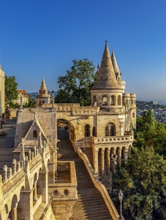 Den ikoniske Fiskerbastionen i Budapests slotskvarter ved solnedgang, med dens karakteristiske hvide stentårne, terrasser og ornamenterede balustrader, der giver en betagende udsigt over Donau og byen