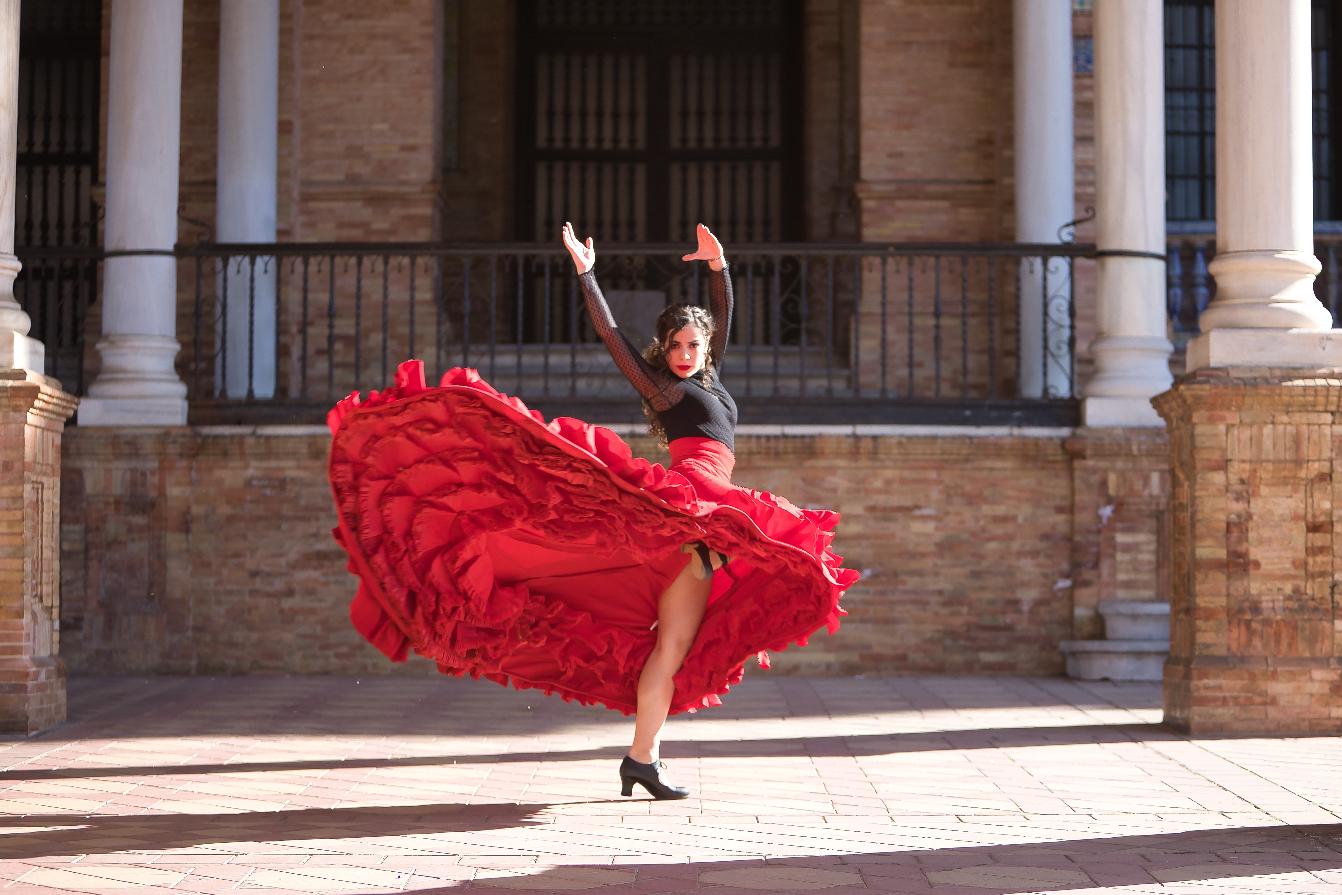 Ung kvinde i dramatisk rød nederdel danser traditionel flamenco mellem marmorsøjler på Plaza de España i Sevilla