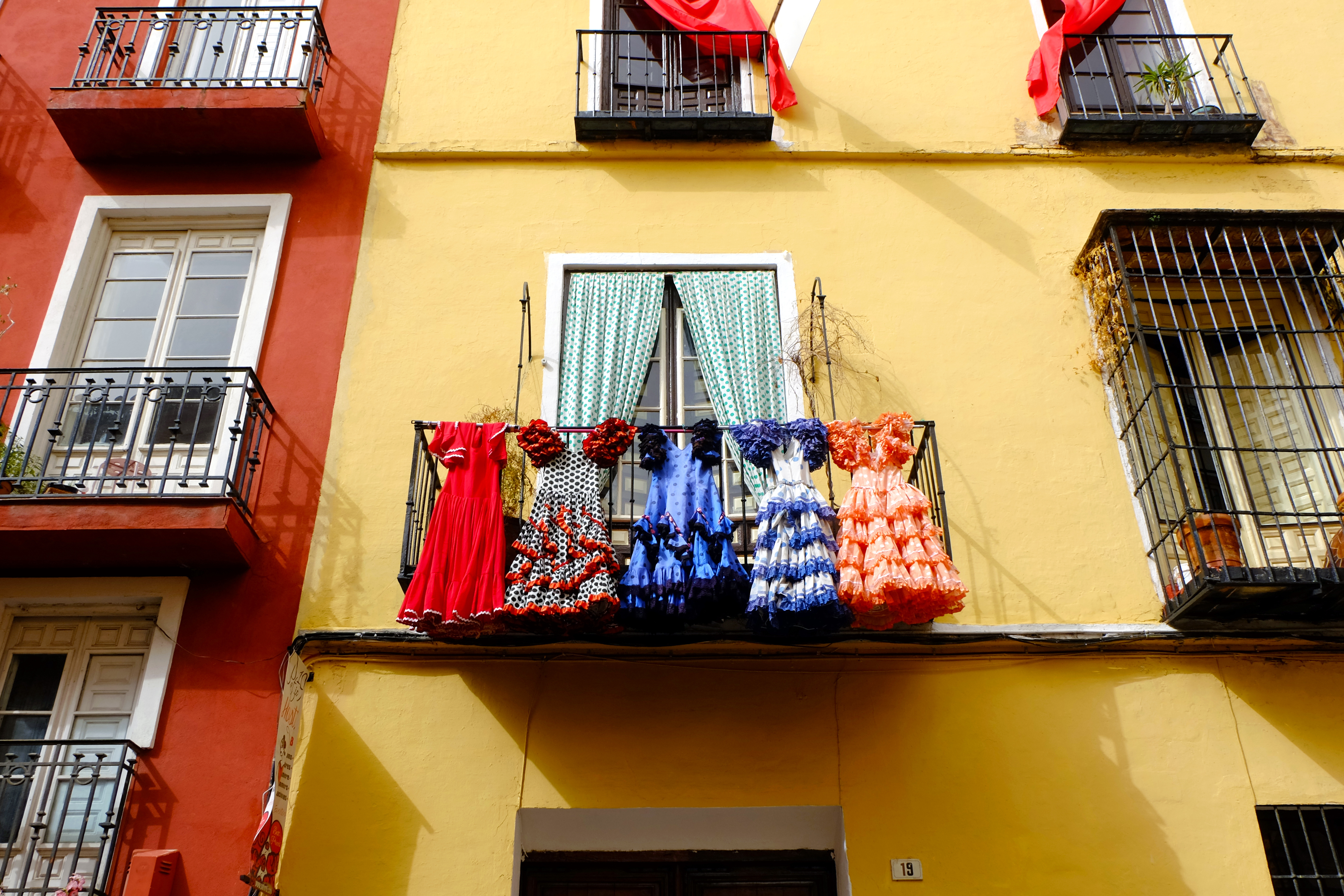 Farvestrålende traditionelle flamenco-kjoler i røde og livlige mønstre, der hænger til tørre på en balkon i Andalusien - et ægte glimt af spansk kultur