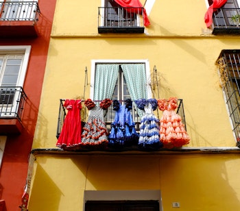 Farvestrålende traditionelle flamenco-kjoler i røde og livlige mønstre, der hænger til tørre på en balkon i Andalusien - et ægte glimt af spansk kultur