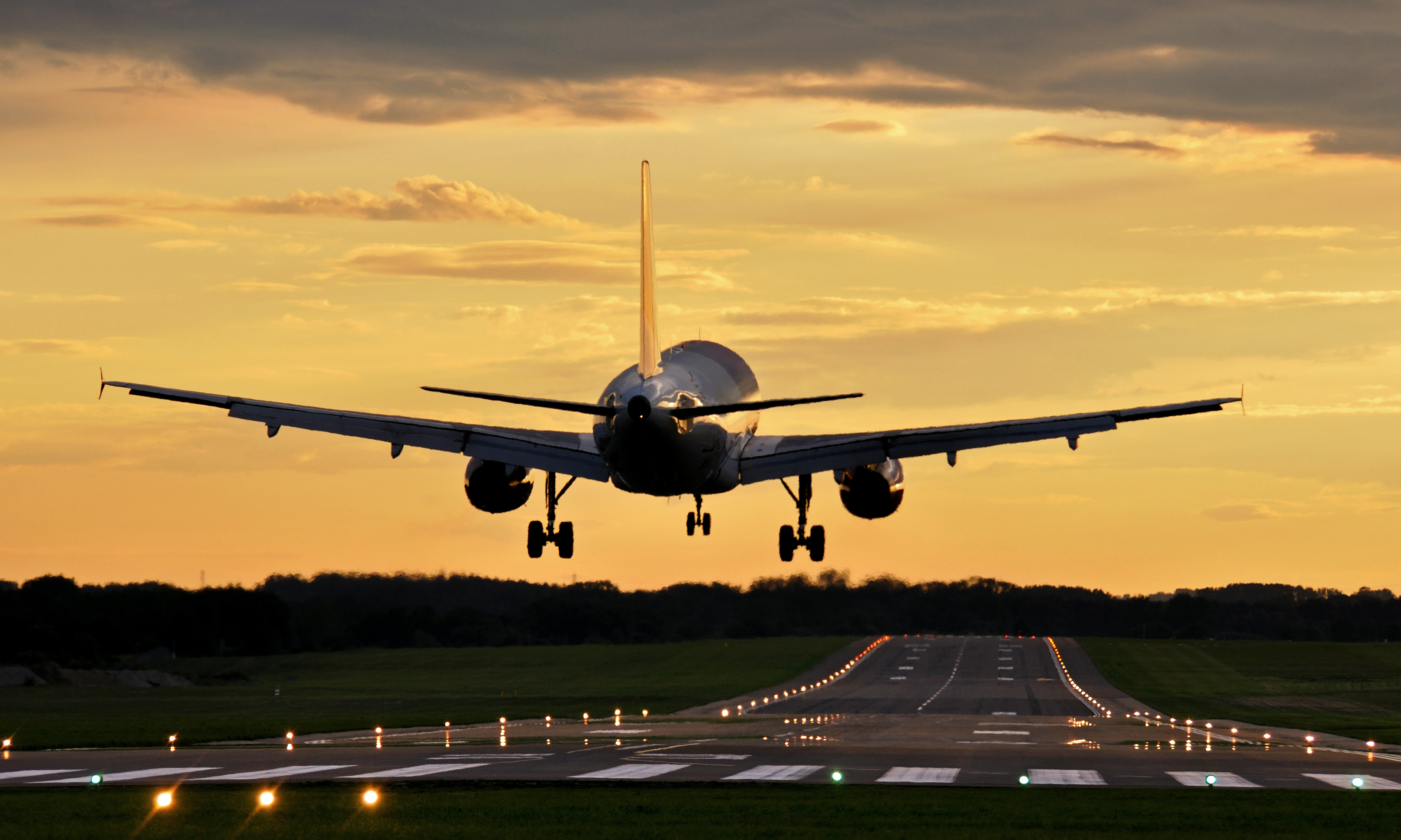 Passagerfly lander på oplyst landingsbane under gylden solnedgang