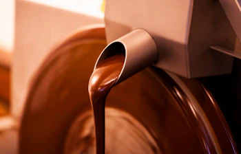 Flydende mørk chokolade der strømmer fra en maskine i en belgisk chokoladefabrik i Bruxelles