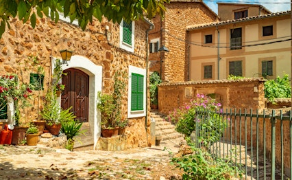 Idyllisk udsigt over den charmerende bjerglandsby Fornalutx på Mallorca med traditionelle stenbygninger, terrakotta-tage og farverige blomsterkrukker langs de snoede brostensbelagte gader